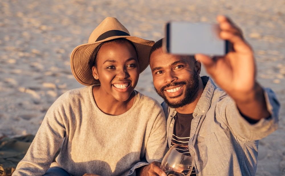 Smiling young African couple sitting together on a sandy beach
