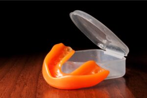 Orange mouthguard near opened case on the wooden texture