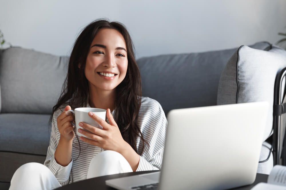 Happy beautiful asian girl drinking coffee and looking at laptop screen