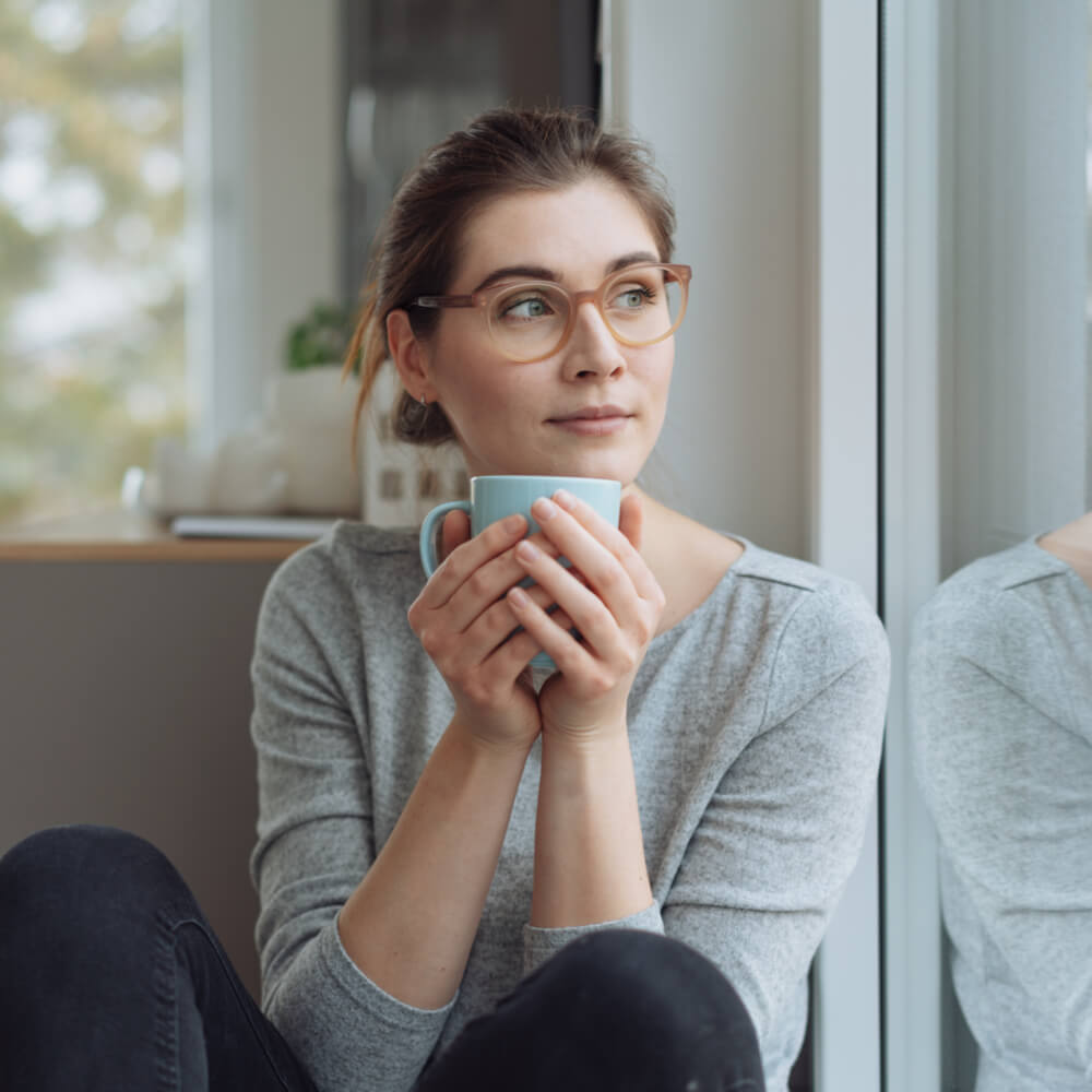 Serious young woman sitting daydreaming with mug of coffee