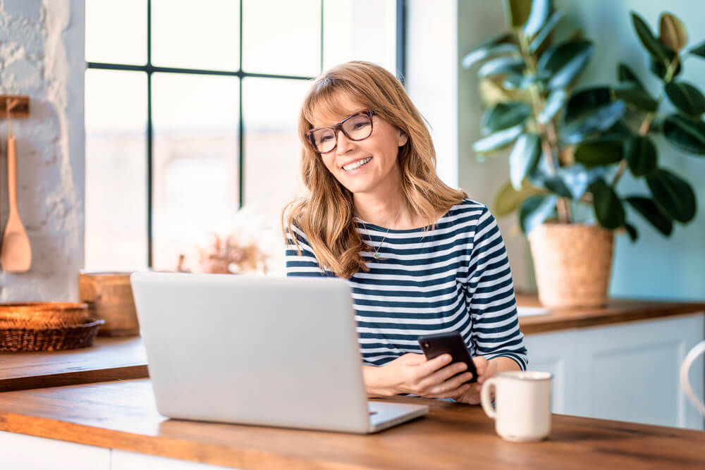 happy woman sitting in the kitchen behind her laptop