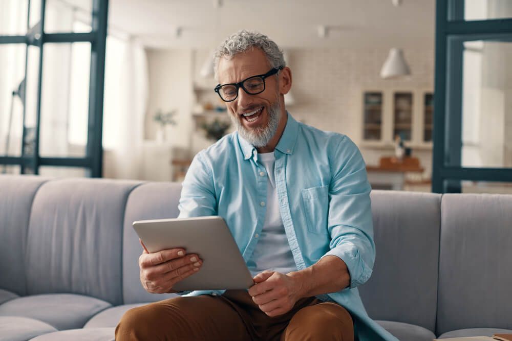Relaxed senior man using digital tablet and smiling while sitting on the sofa