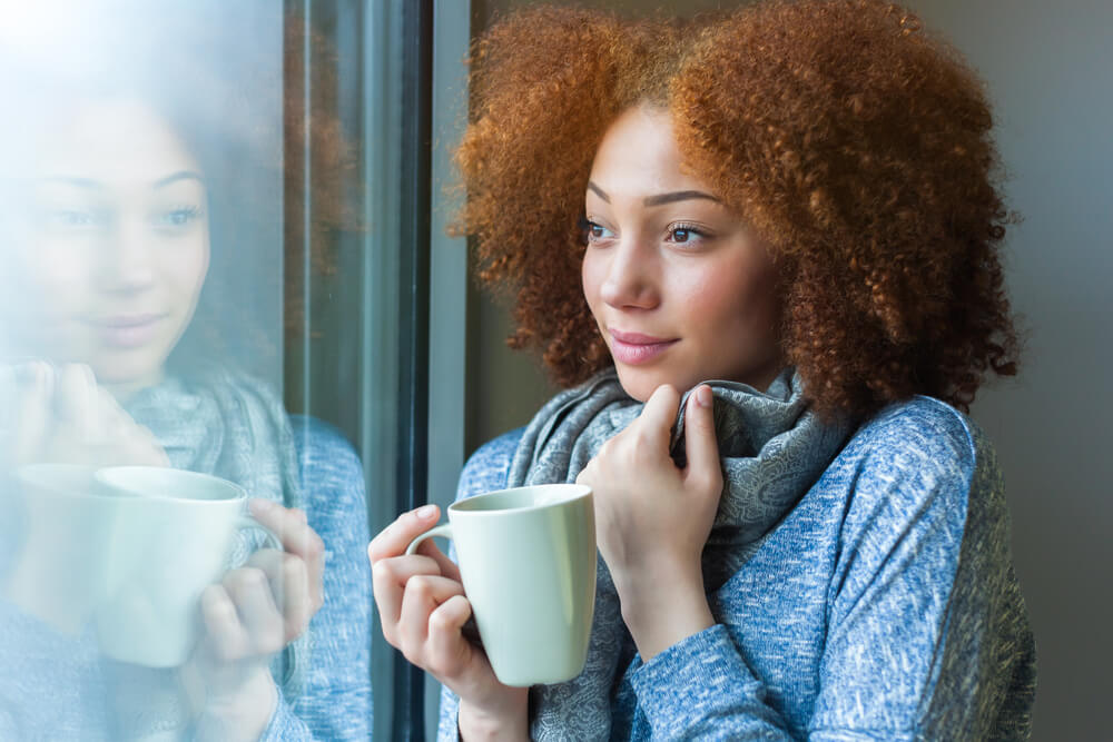 Black African American teenage girl drinking a hot beverage and looking through a window