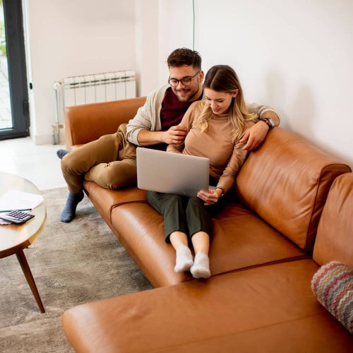 Handsome young couple using laptop together while sitting on sofa at home