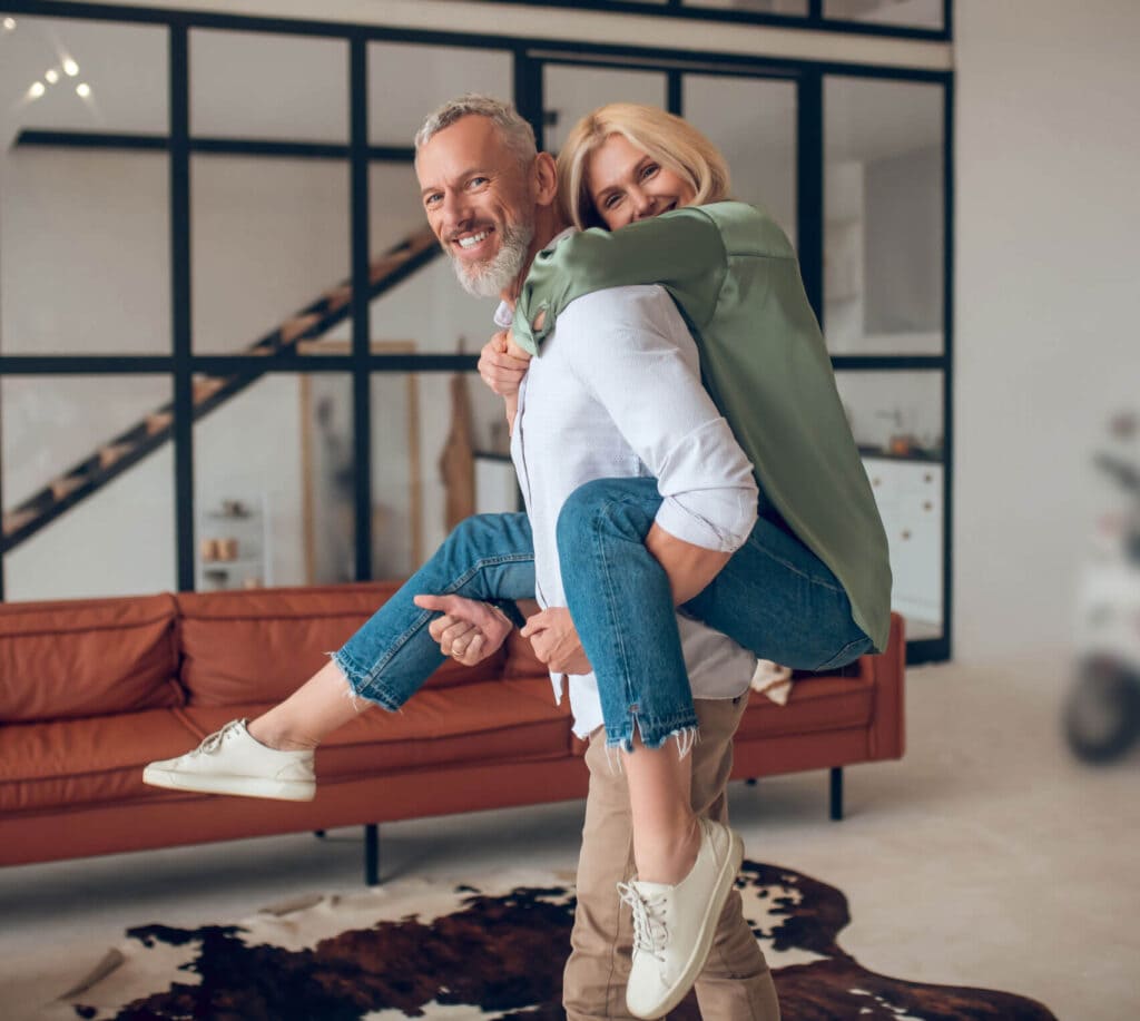 Happy couple. Man holding his wife on his back and both feeling wonderful