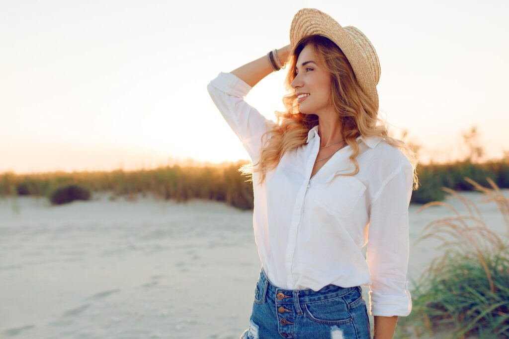 smiling woman in white blouse and straw hat spending time on the beach