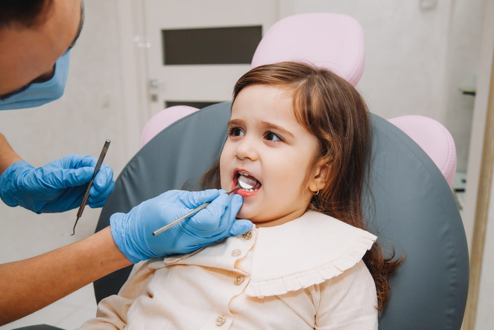 dentist, doctor examines the oral cavity of a little girl, uses a mouth mirror, baby teeth close-up