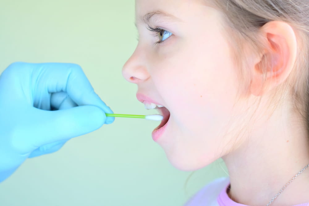 pediatrician using a cotton swab to take a sample from a girl throat