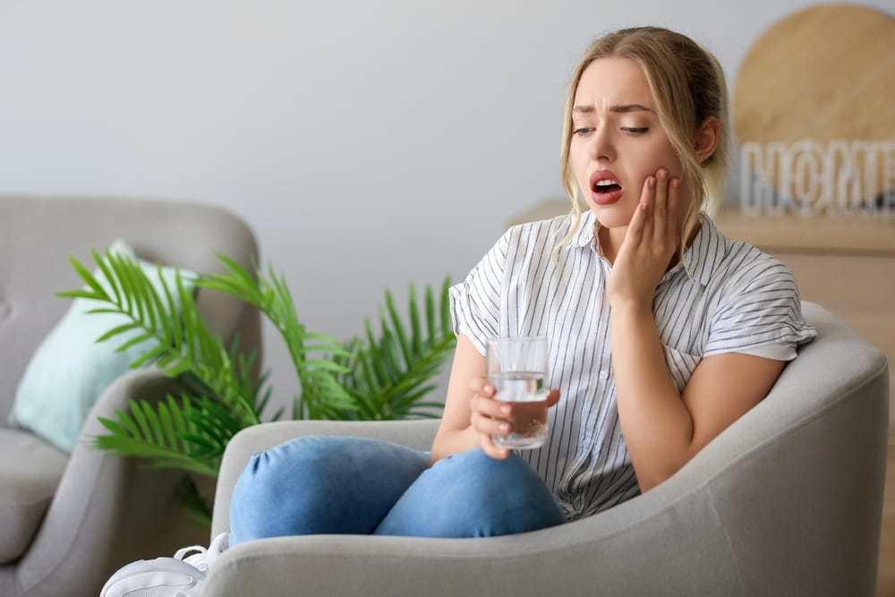 Young woman with dissolved tablet in glass of water suffering from toothache at home