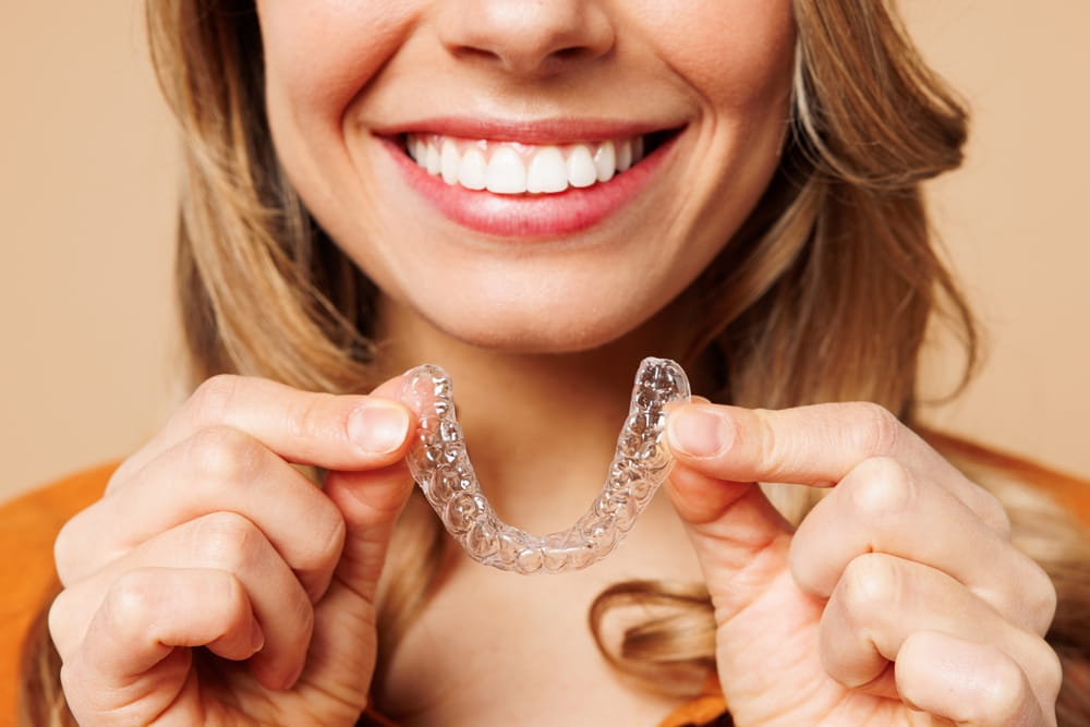 Close up cropped young woman wear orange shirt casual clothes hold in hand invisible transparent aligners, invisalign bracer smile
