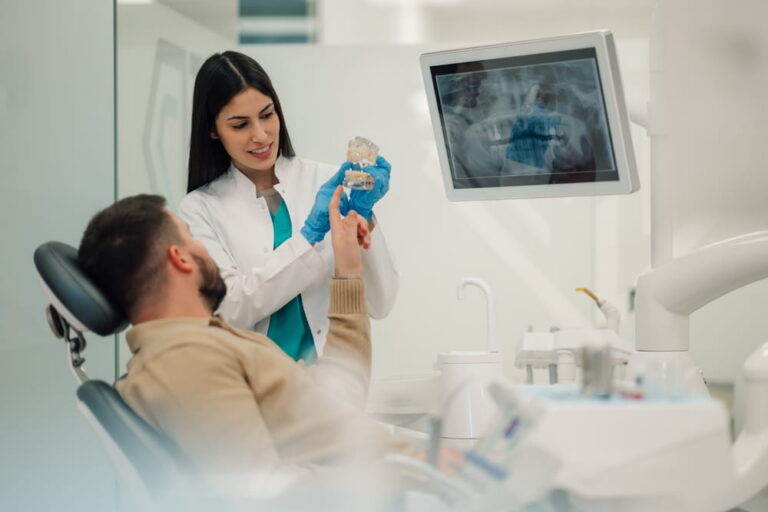Female dentist is showing a teeth model to a male patient during a consultation in a modern dental clinic.