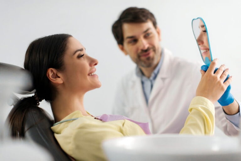 Happy woman patient smiling and looking at her reflection in mirror while sitting in dental chair, satisfied with result
