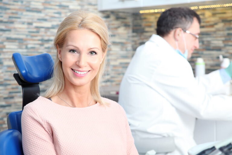Portrait of beautiful middle age woman sitting at dentistry while male dentist working at background.