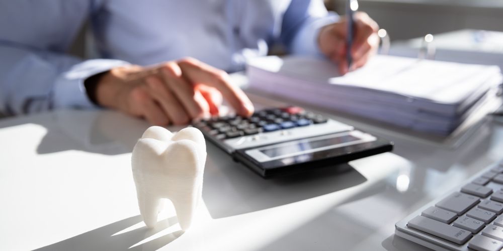 Close-up Of Tooth In Front Of Businessperson Calculating Bill