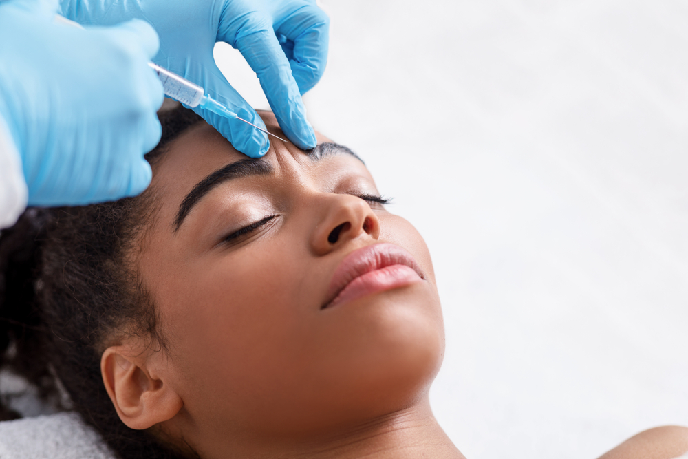 Plastic Surgery. Young African Woman Receiving Botox Injection In Interbrow