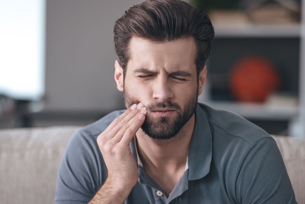 Toothache. Frustrated Young Man Touching His Cheek And Keeping Eyes
