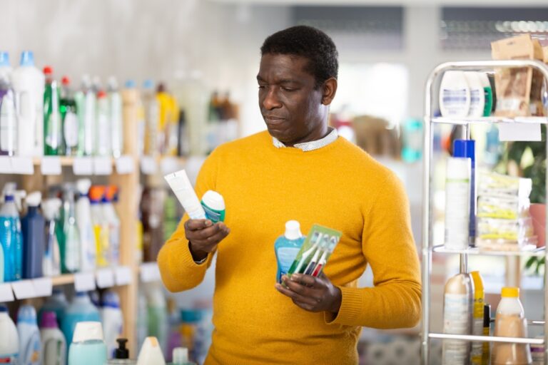Male shopper chooses best toothbrush and toothpaste in supermarket