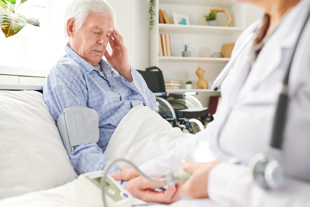 Unwell aged patient of hospital with headache or high blood pressure sitting in bed while doctor checking it up