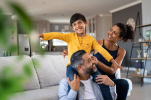 Cheerful son sitting on father shoulder playing at home with mother.