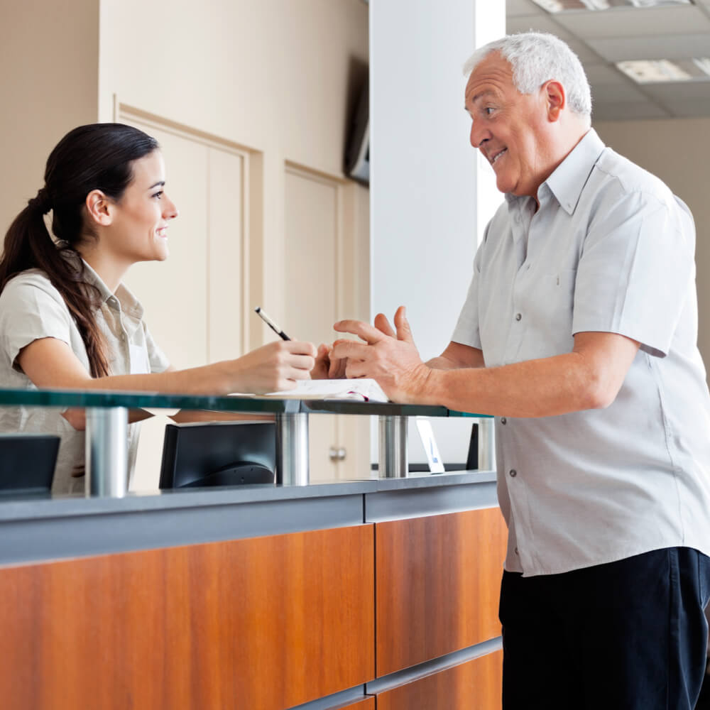 Senior man communicating with female receptionist while women sitting in background