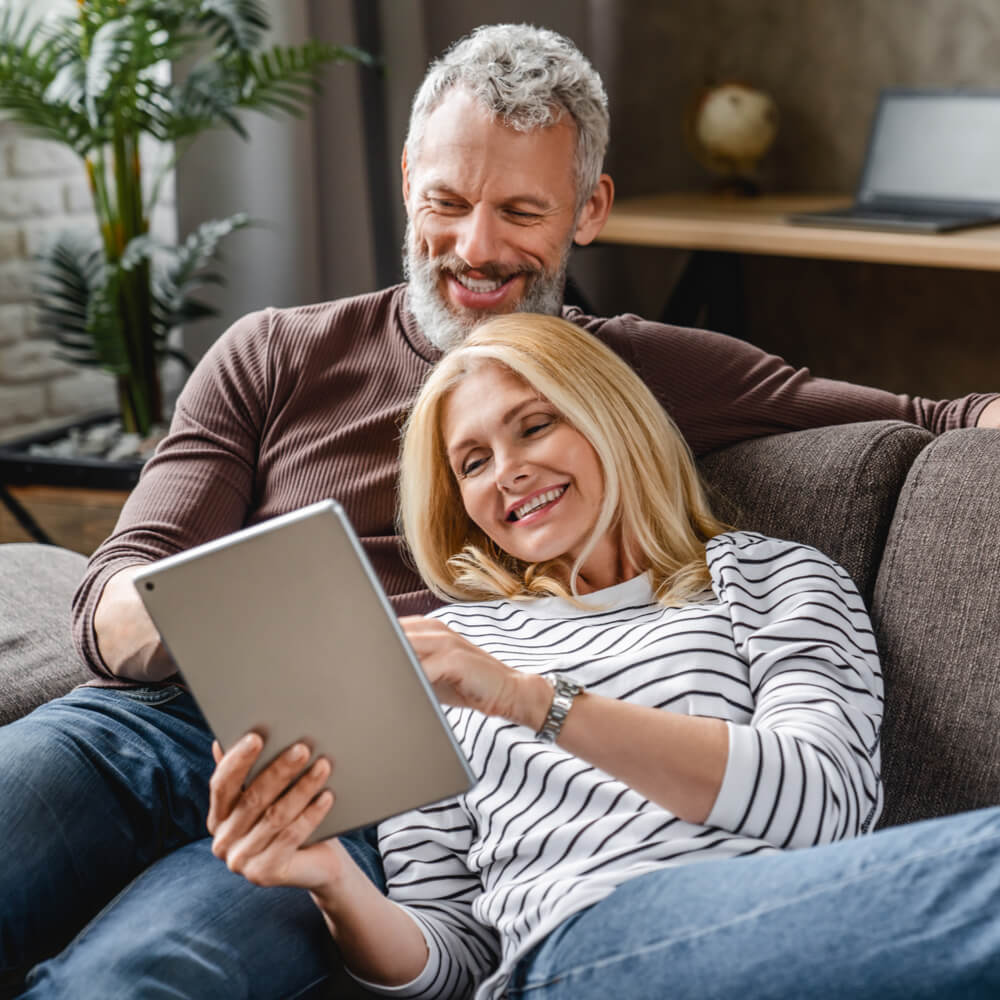 Happy senior couple using digital tablet on sofa indoors