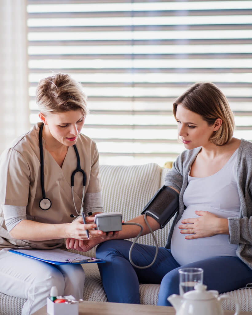 A healthcare worker examining pregnant woman indoors at home.