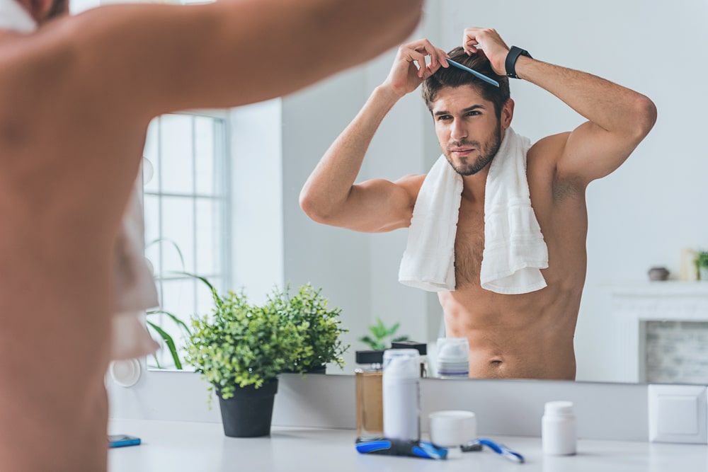 Young fit man looking in mirror with towel on neck