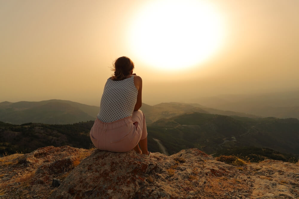 Back view of a woman alone contemplating sunset in the mountain