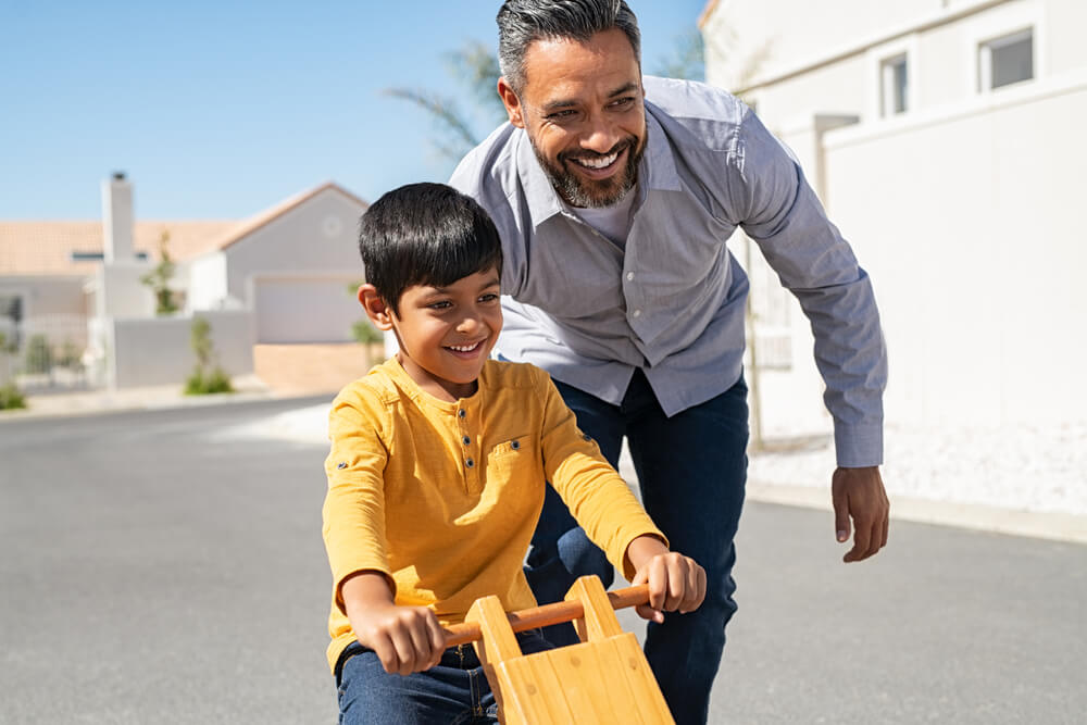 Cheerful father helping excited son to ride wooden cycle